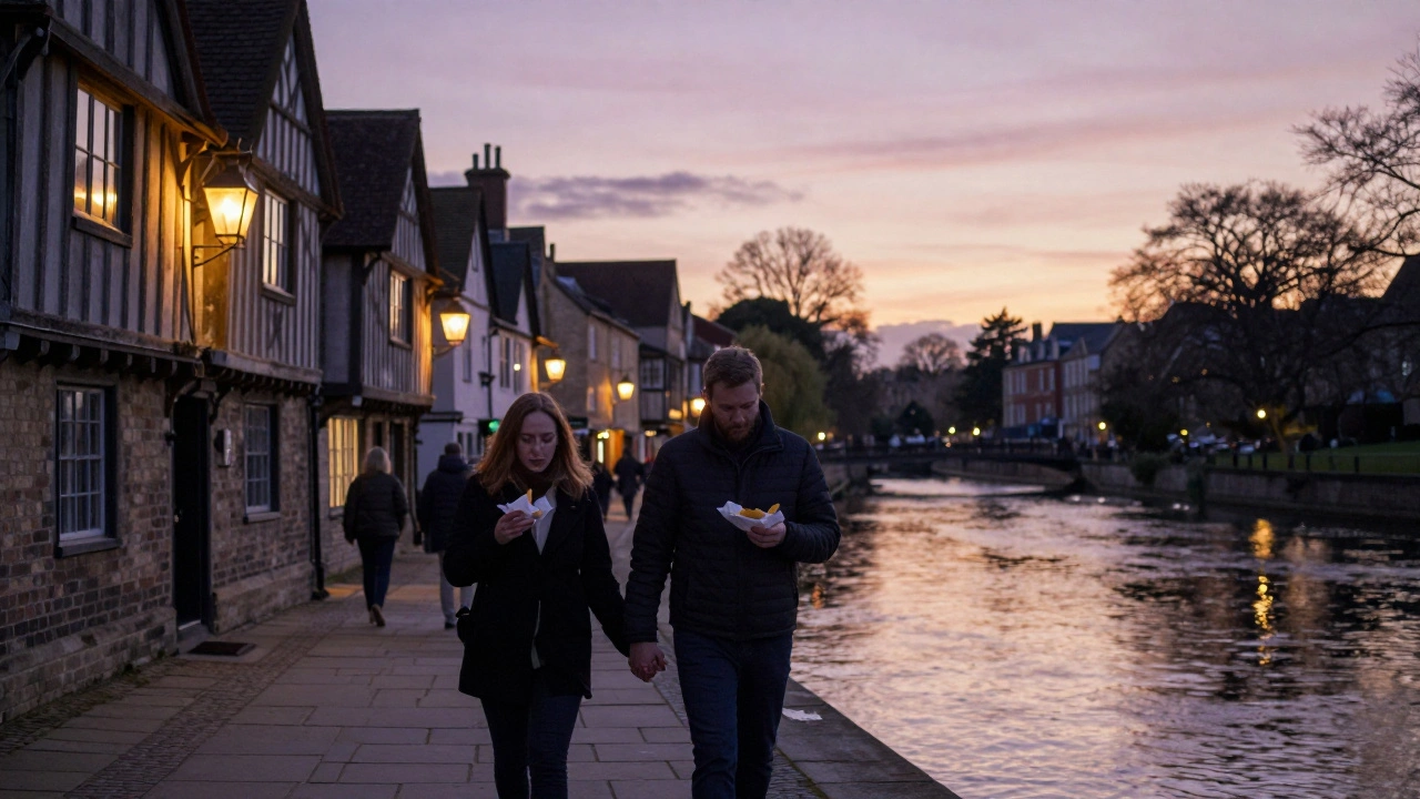A couple walking hand-in-hand along a river in York, eating fish and chips under lantern-lit medieval buildings.